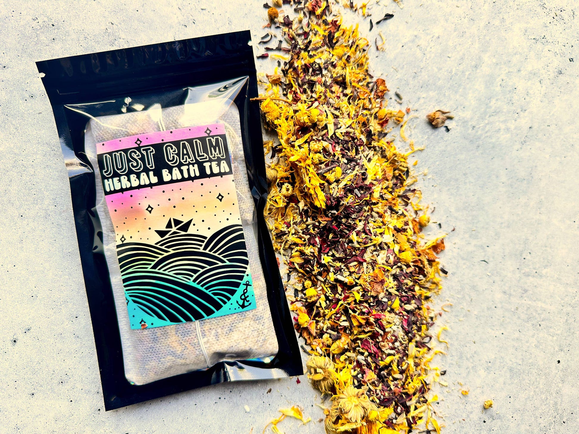 Packaged 'Just Calm Herbal Bath Tea' with a scattering of tea leaves on a textured surface.