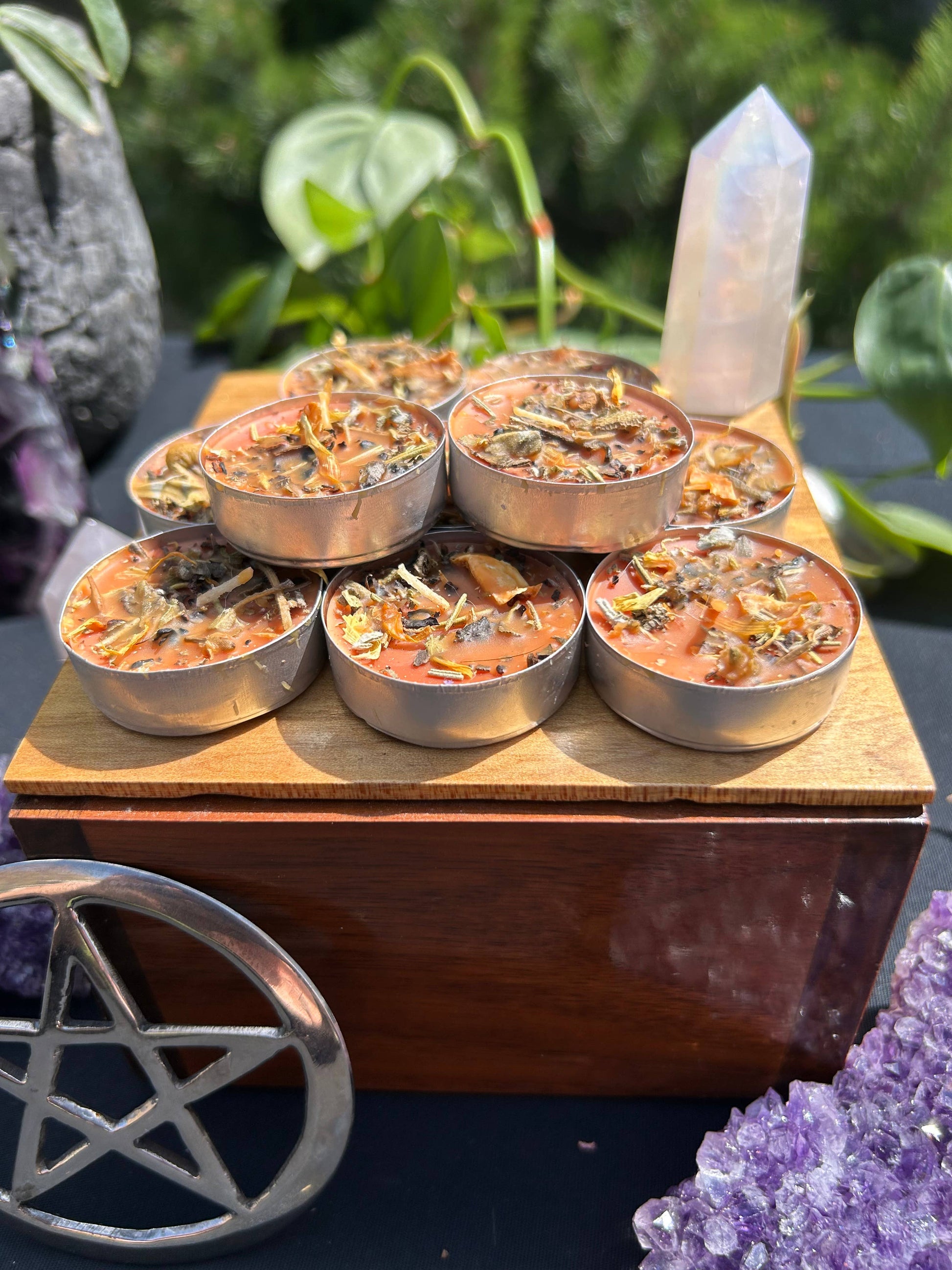 Set of small candles in metal containers on a wooden stand with crystals and plants in the background.