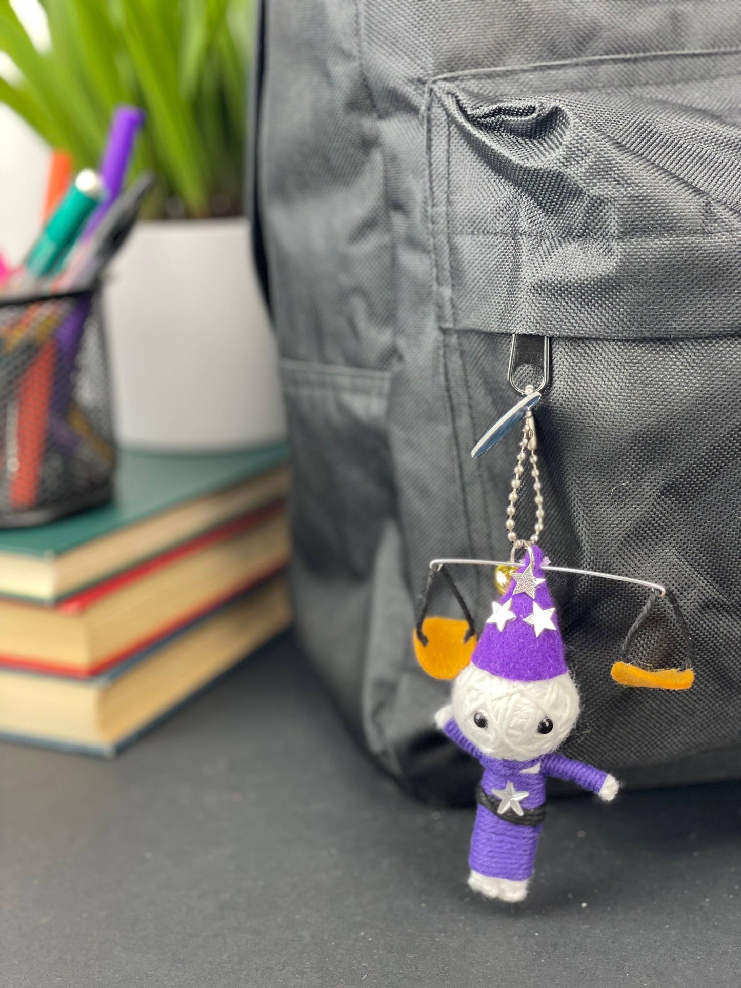 Small wizard figurine keychain on a backpack with books and stationery items in the background.