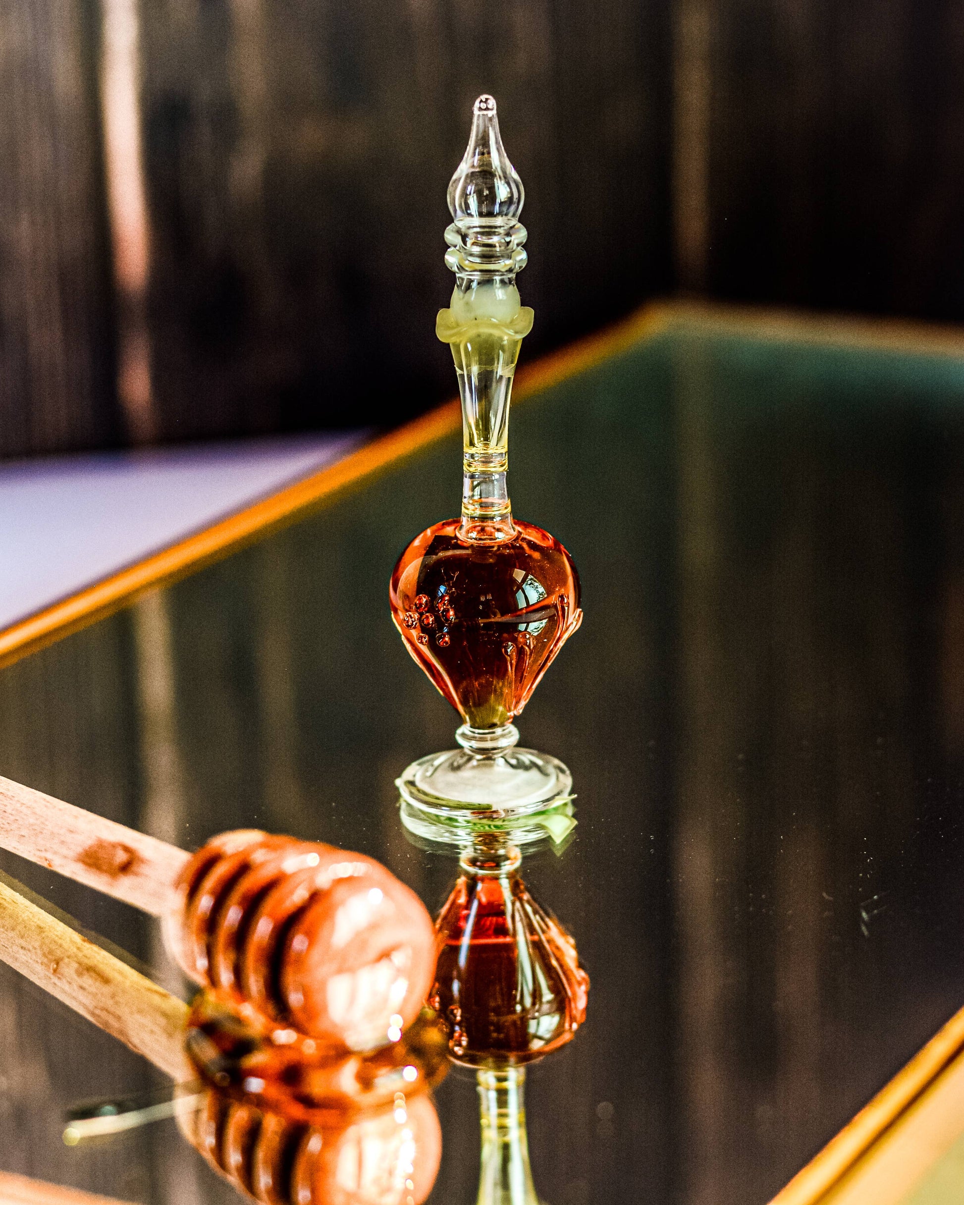 Glass honey dipper with honey on a reflective surface