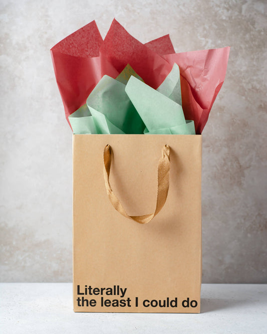 Brown paper bag with colorful tissue paper and humorous text on a neutral background
