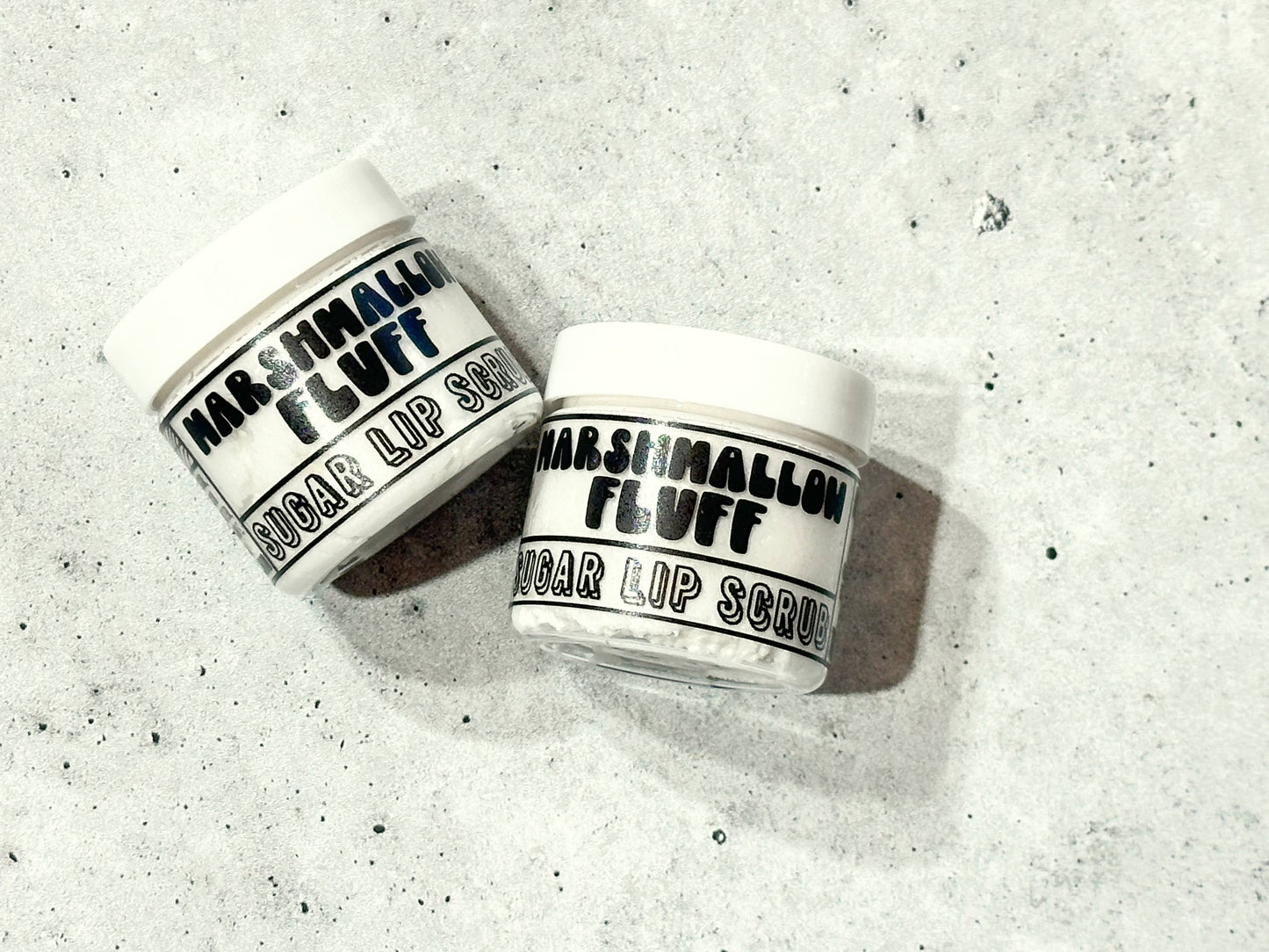 Two jars of Marshmallow Fluff lip scrub on a textured gray surface