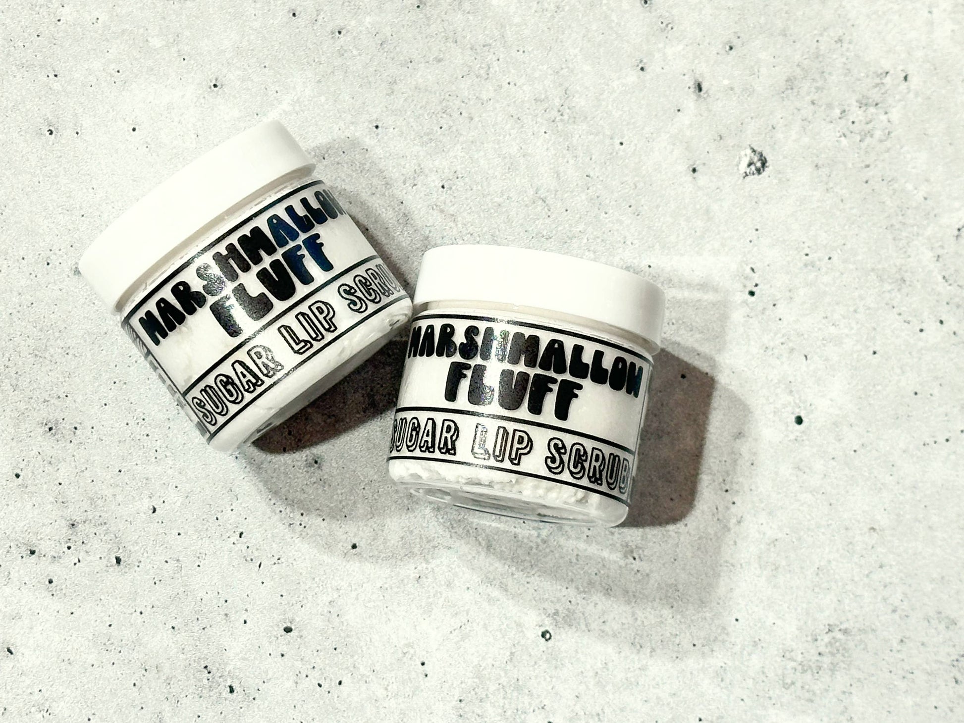 Two jars of Marshmallow Fluff lip scrub on a textured gray surface