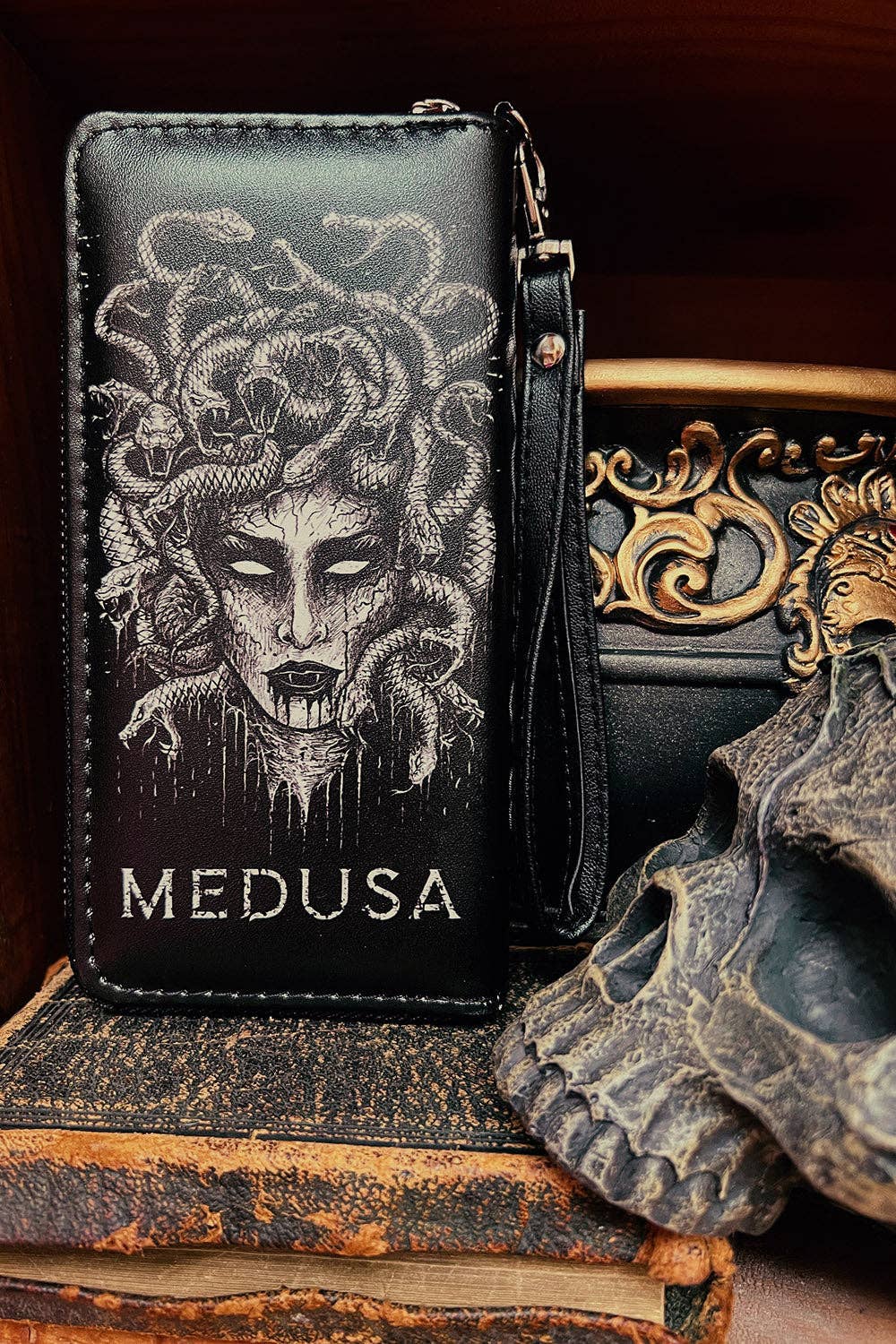 Black leather wallet featuring a detailed white illustration of Medusa and the word 'MEDUSA' printed in white, displayed on a stack of vintage books next to a skull prop.