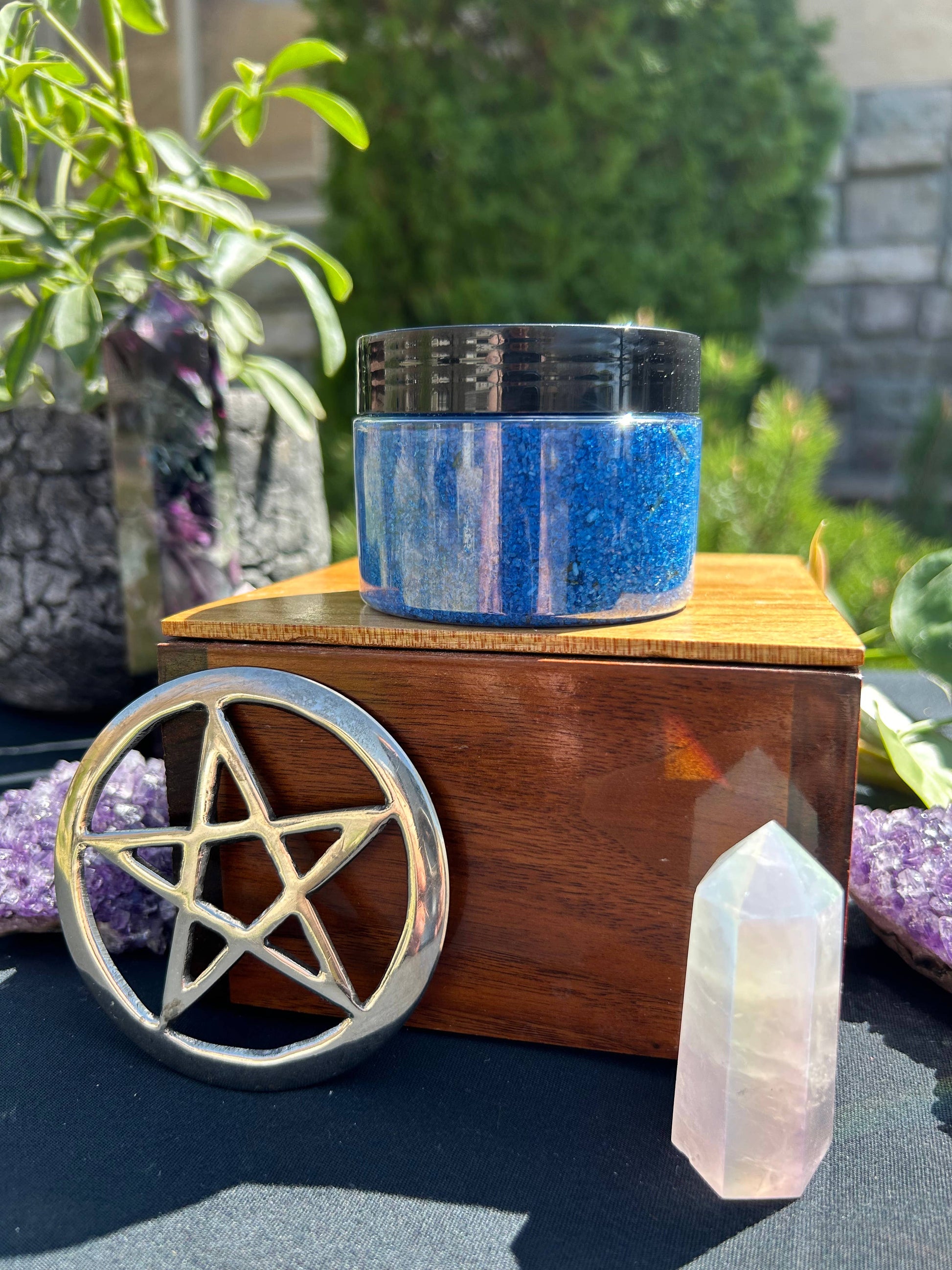 Wooden box with a pentagram symbol, container of blue powder, and crystal on a natural background