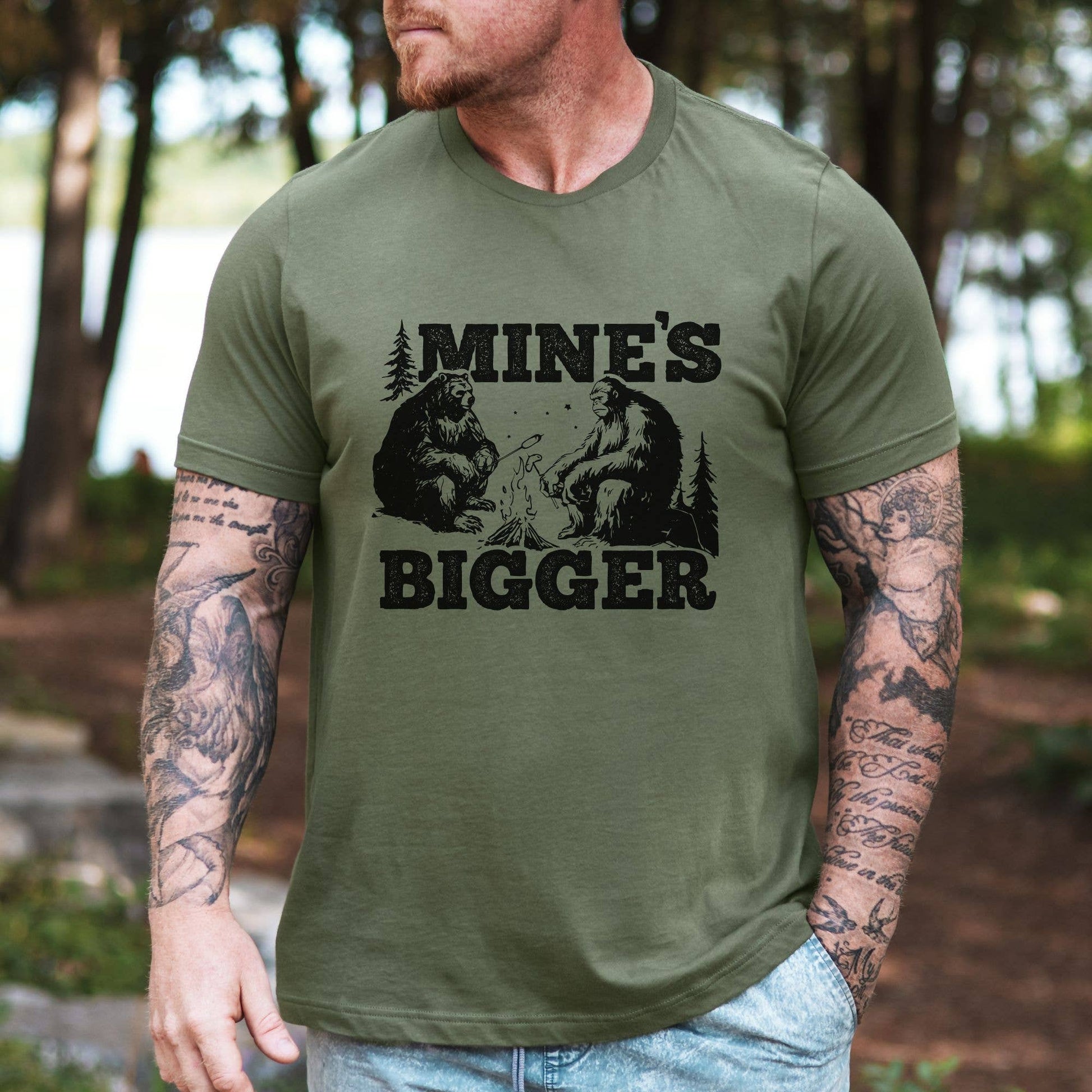 Man wearing a green t-shirt with 'MINE'S BIGGER' graphic and bear design outdoors.