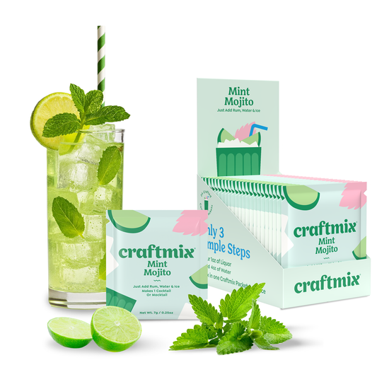 Glass of mint mojito with lime slices and mint leaves, surrounded by craftmix Mint Mojito packets.
