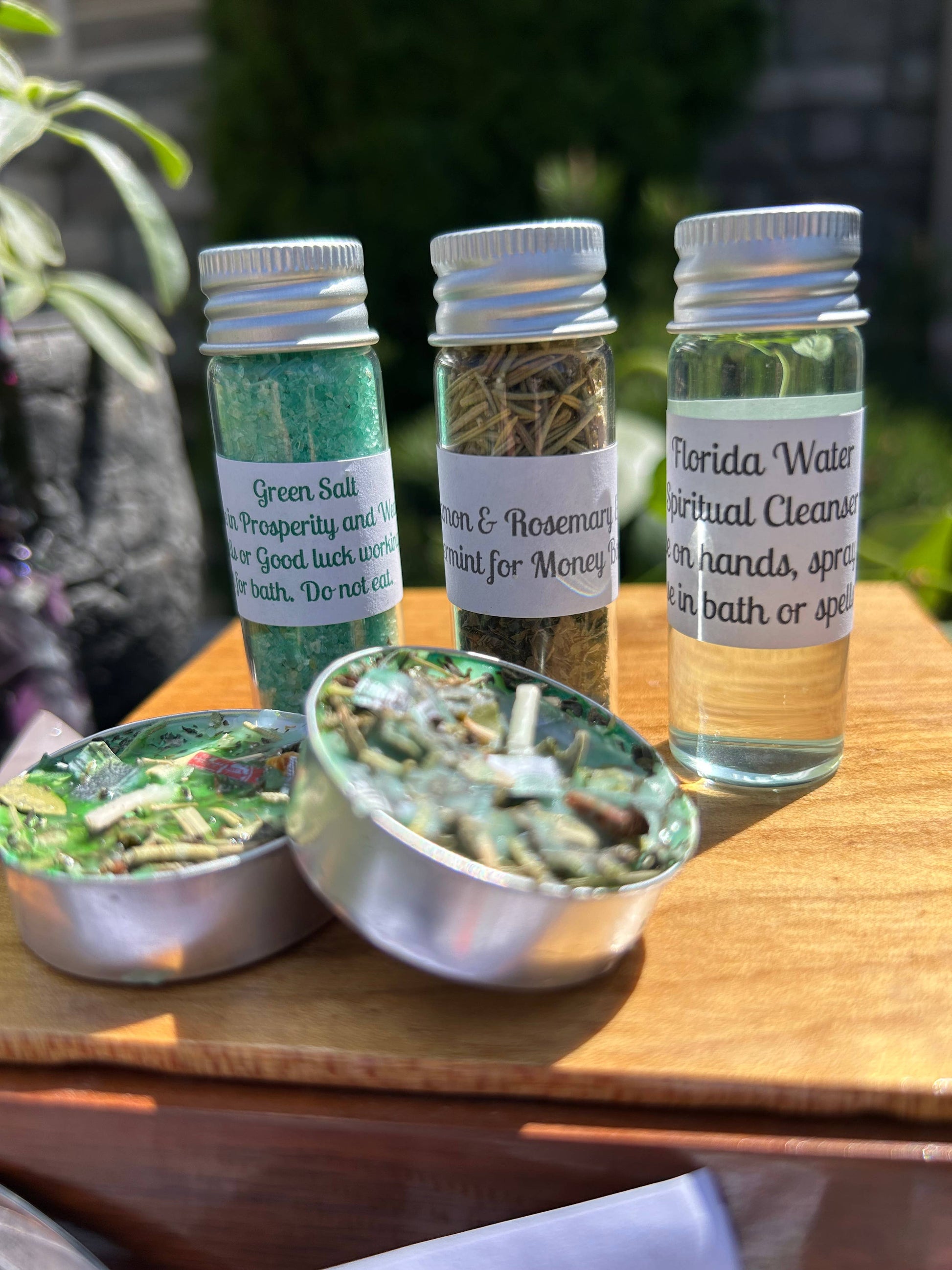 Three bottles with labels and two metal containers filled with green and brown substances on a wooden surface.