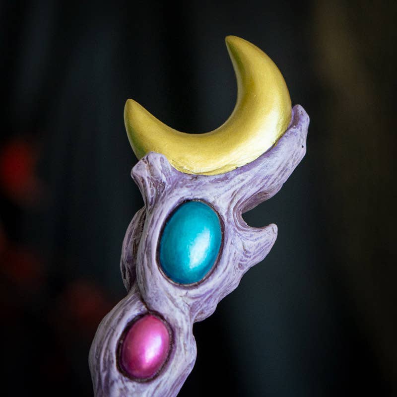 Decorative staff with moon, turquoise, and pink accents on a dark background