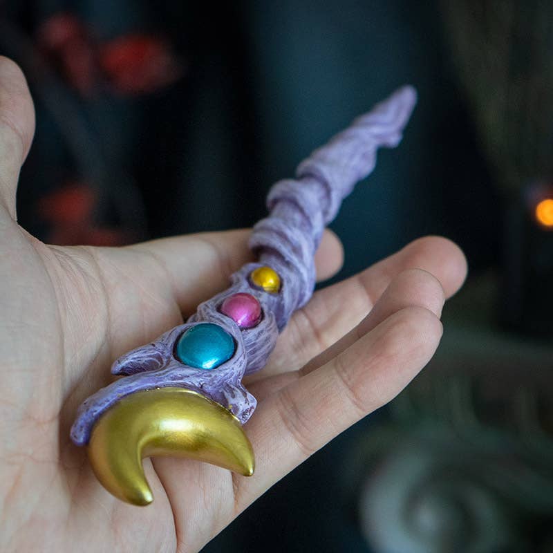 Hand holding a colorful staff with gemstones against a blurred background
