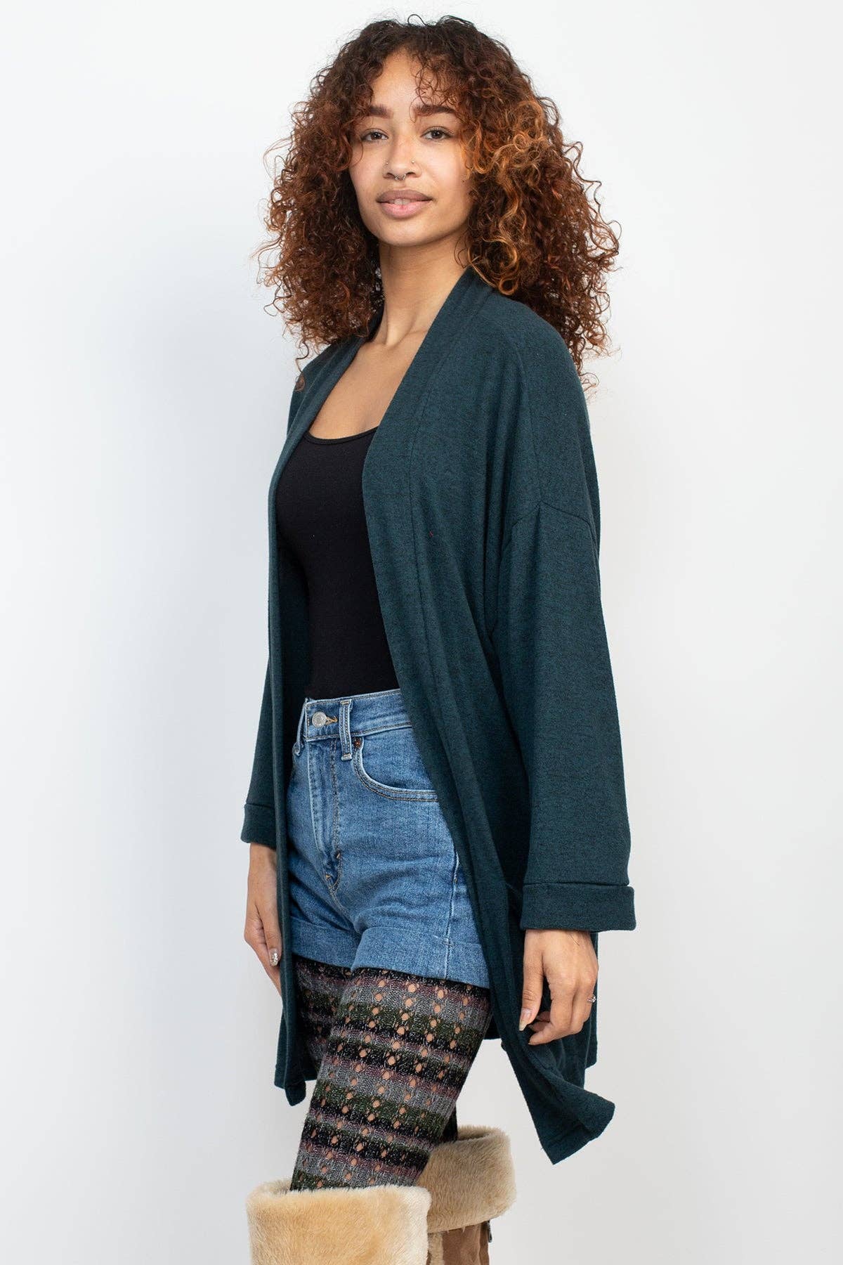 Woman wearing a teal cardigan over a black top and jeans, standing on a white background