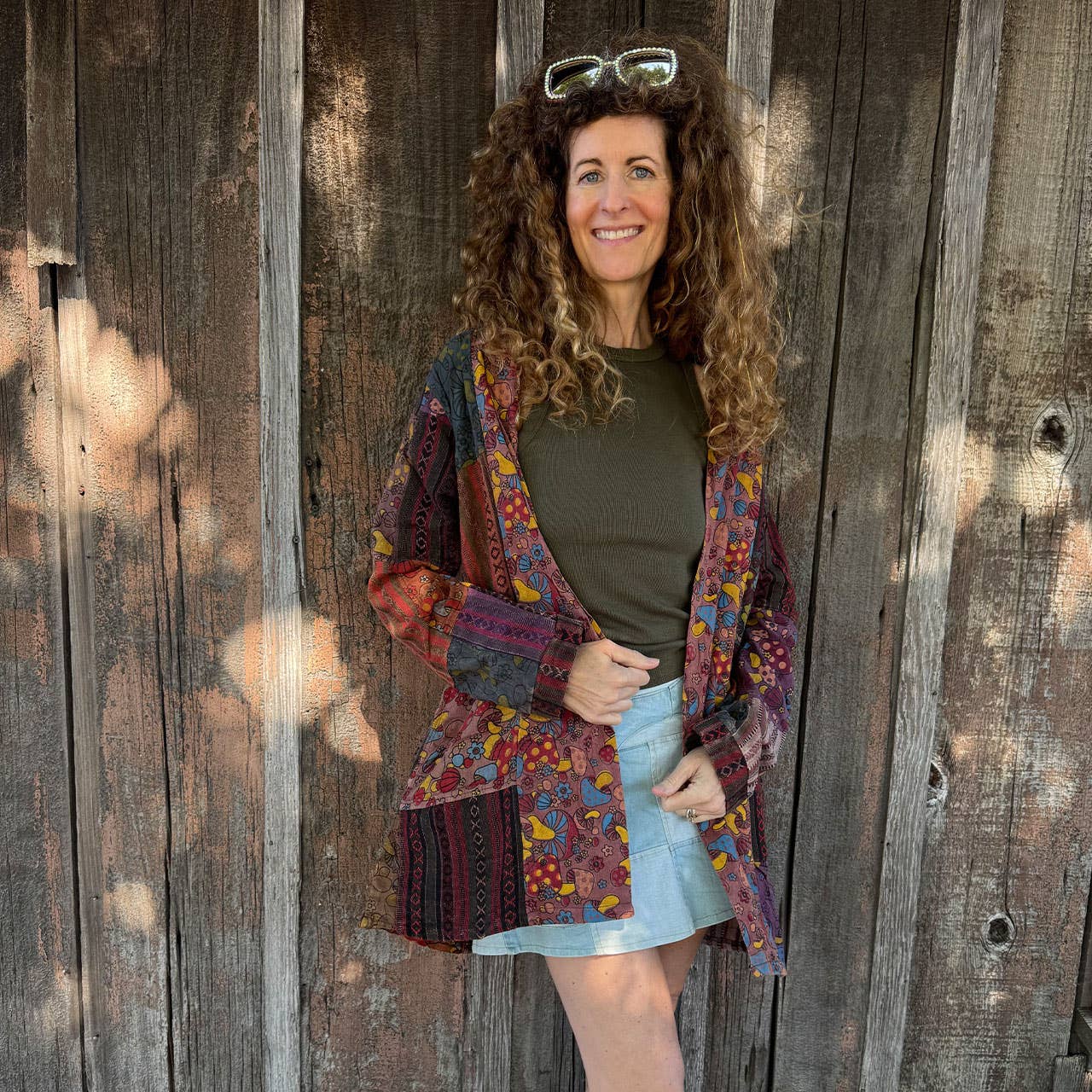 Woman wearing a colorful patchwork jacket standing in front of a wooden wall.