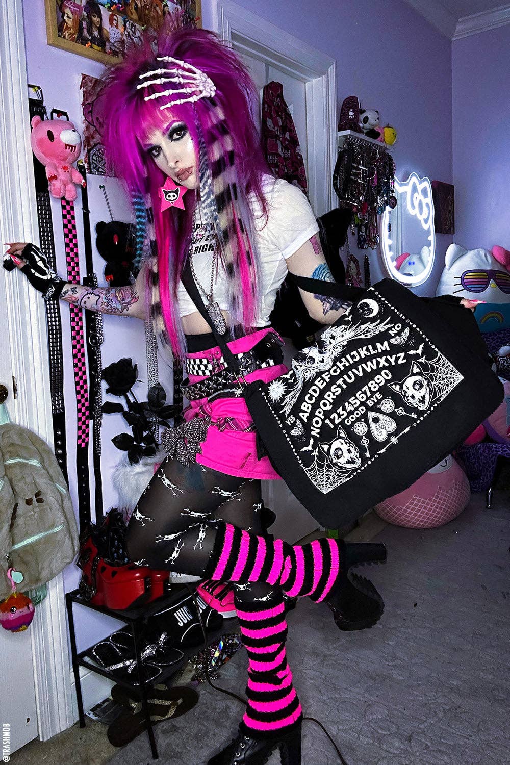 Person with vibrant pink hair and gothic attire in a room with various decorations.