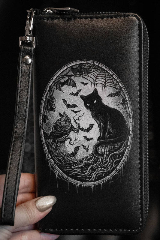 Black wallet with a black cat and bats design held by a hand against a dark background