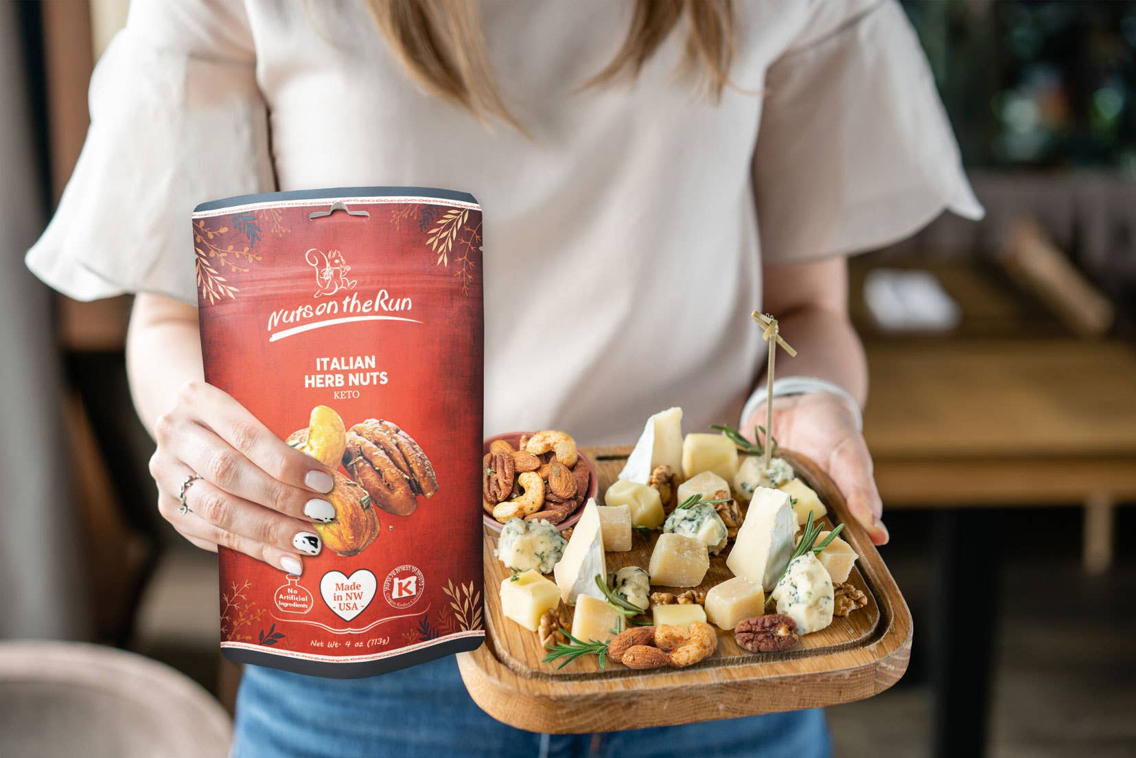Person holding a can of 'Between the Run' Italian Herb Nuts and a platter of cheese and nuts.
