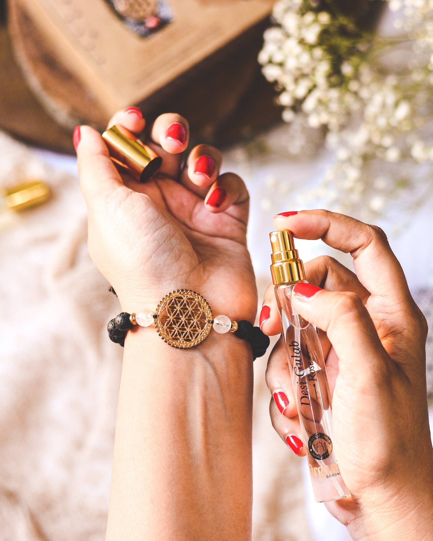 Two hands holding a perfume bottle and a bracelet with a floral design.