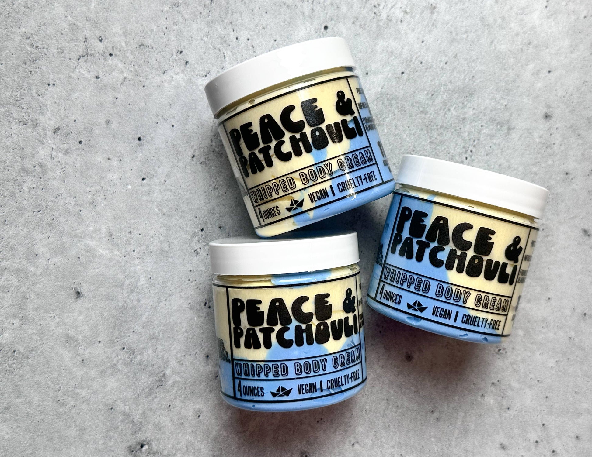 Three jars of Peace & Patchouli whipped body cream on a concrete surface