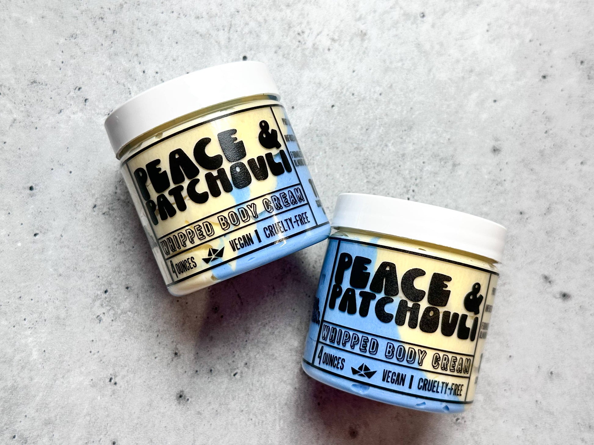 Two jars of Peace & Patchouli whipped body cream on a textured surface