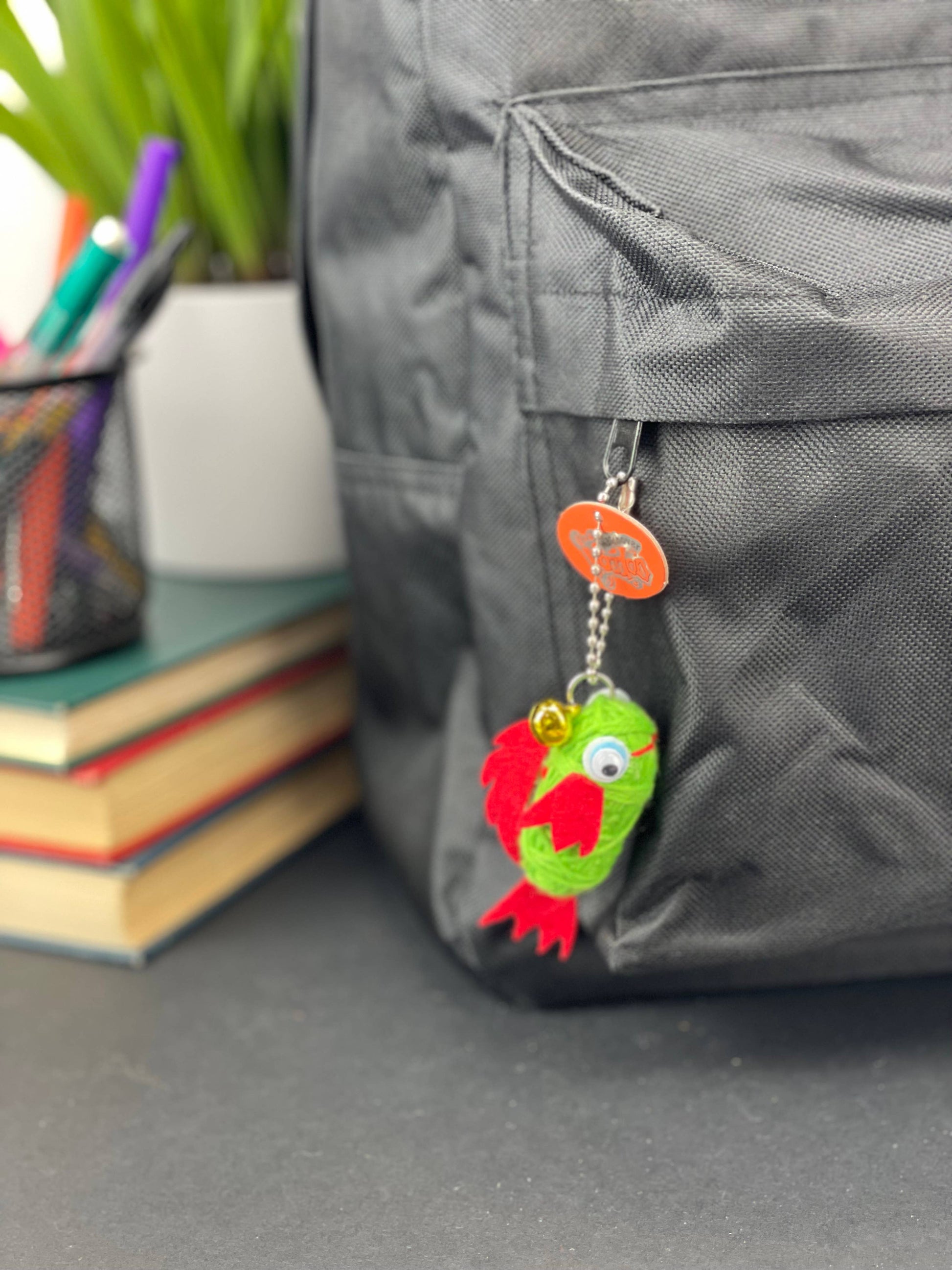 Colorful keychain attached to a gray backpack with books and stationery items in the background.