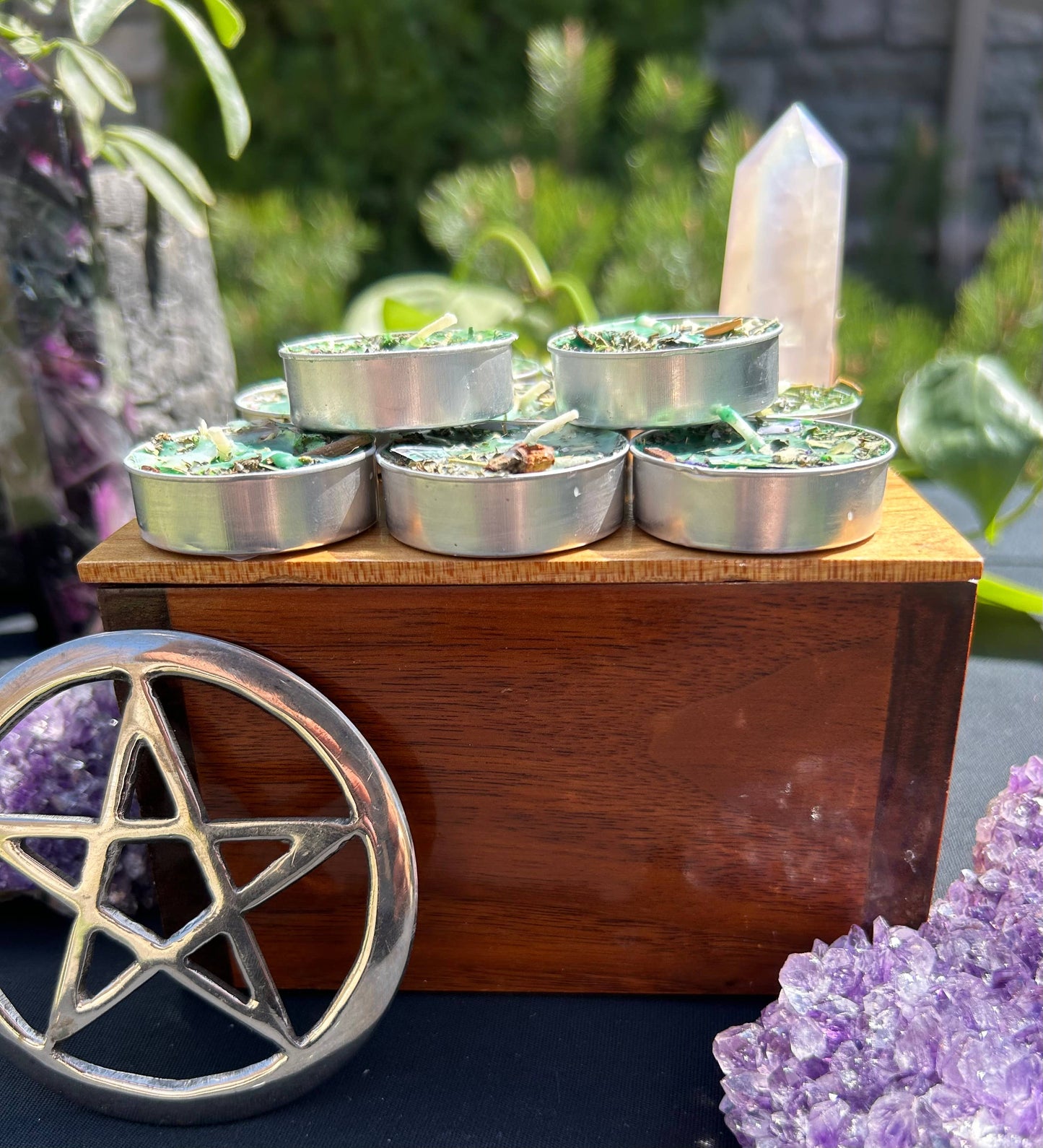 Set of small metal containers with candles on a wooden stand, surrounded by crystals and plants.
