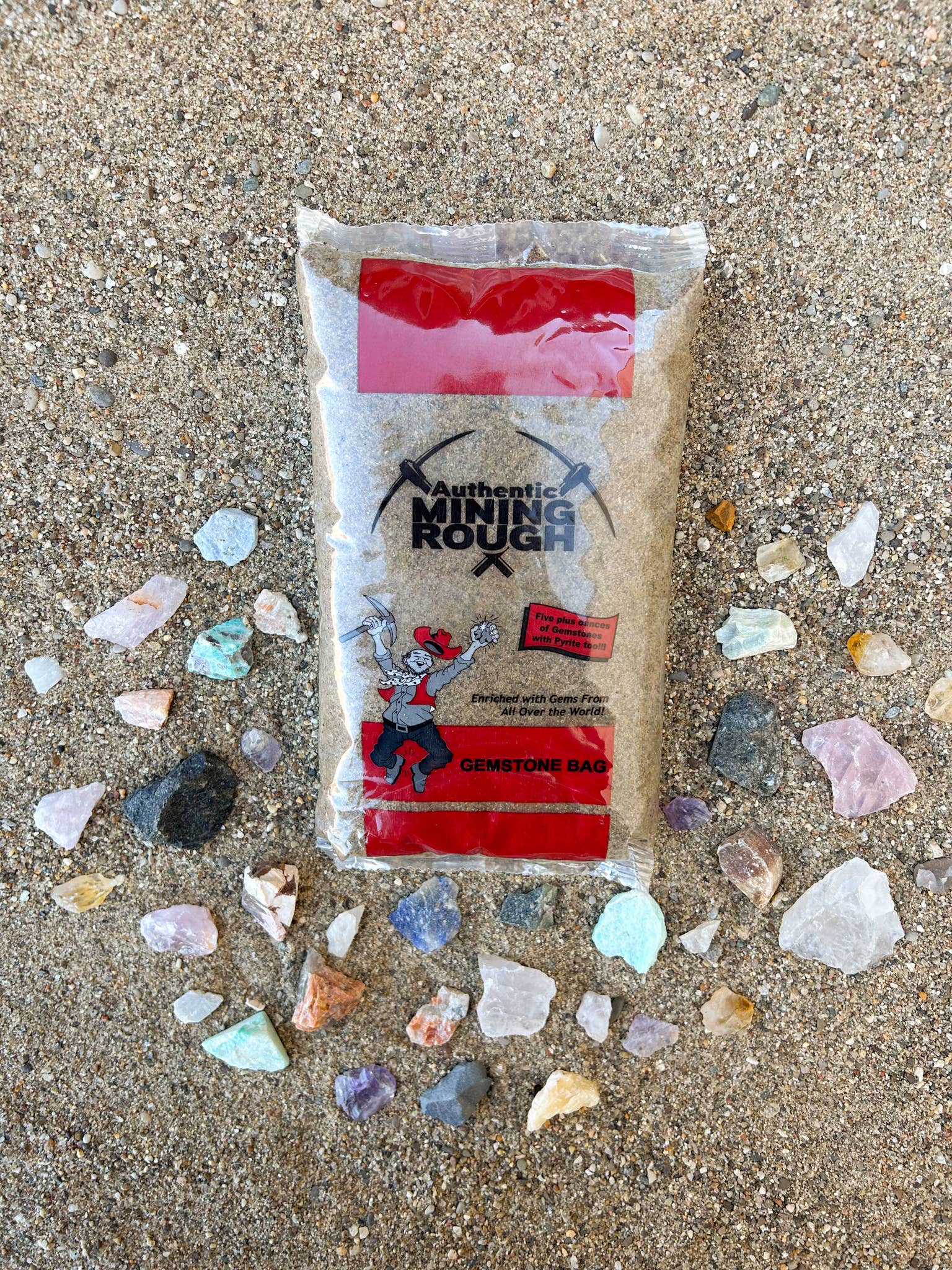 Packaged product with 'Authentic Mining Rough' label on a sandy surface with small stones.