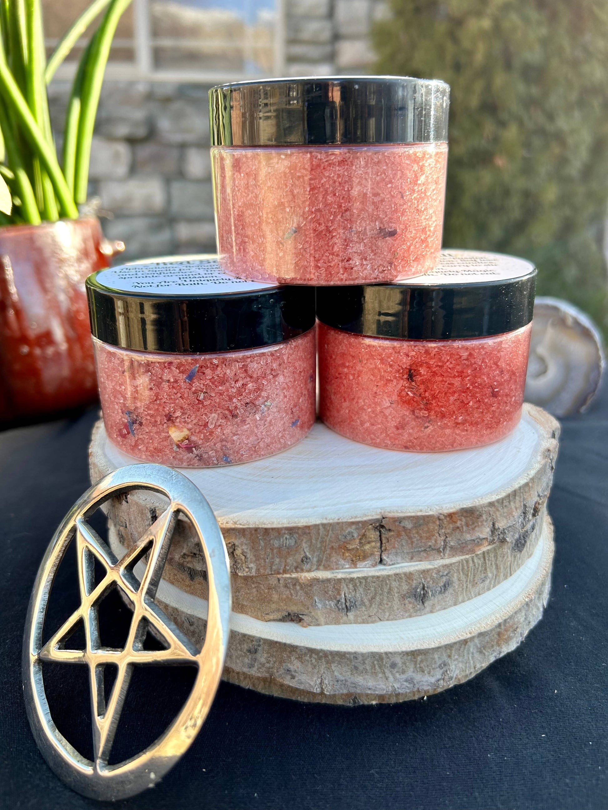 Three jars of a red and black product on a wooden stand with a pentagram symbol in the foreground.