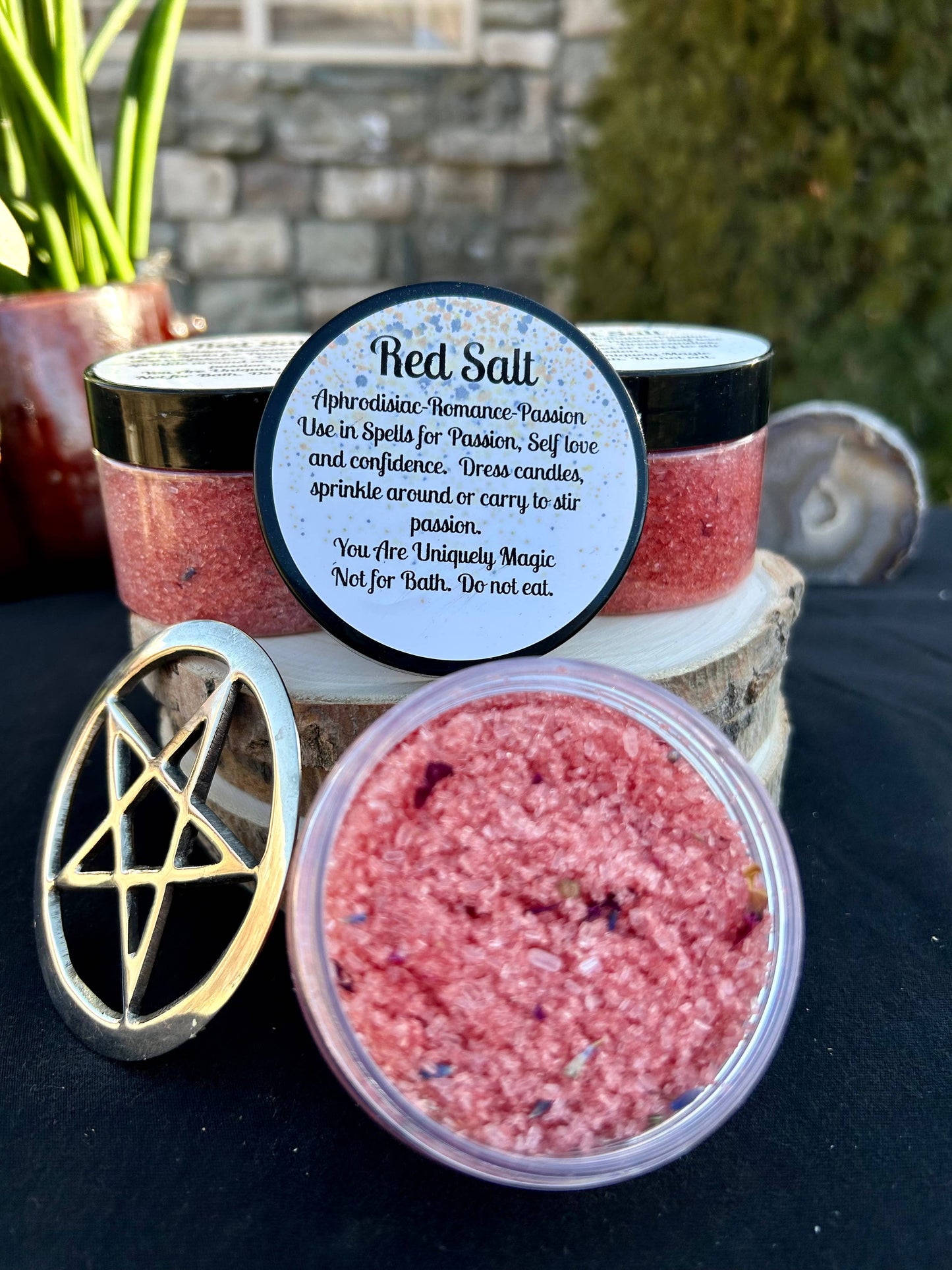 Red salt in a container with a pentagram symbol and a label on a dark surface.