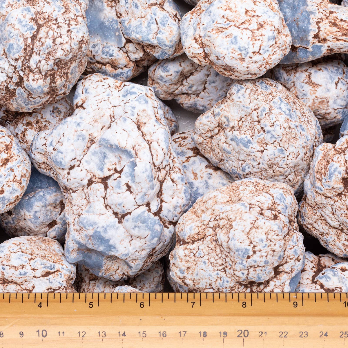 A pile of rough, textured decorative rocks or gravel pieces in mottled light blue and beige tones, with a wooden ruler at the bottom showing measurements for scale.