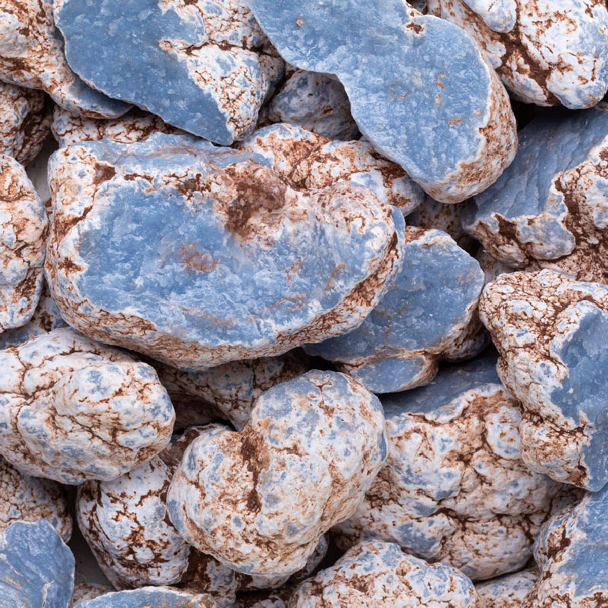 A close-up pile of irregular decorative stones or rocks with a mottled finish, showing light blue surfaces mixed with white and warm brown speckling.