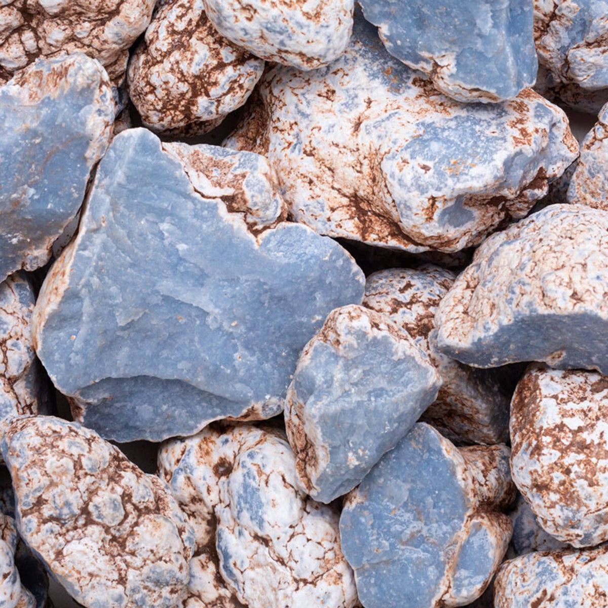 A close-up pile of rough decorative stones and gravel in muted blue-gray and warm beige-brown tones.