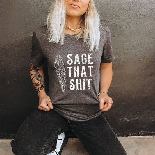 Person wearing a brown t-shirt with 'SAGE THAT SHIT' text and feather graphic against a dark background