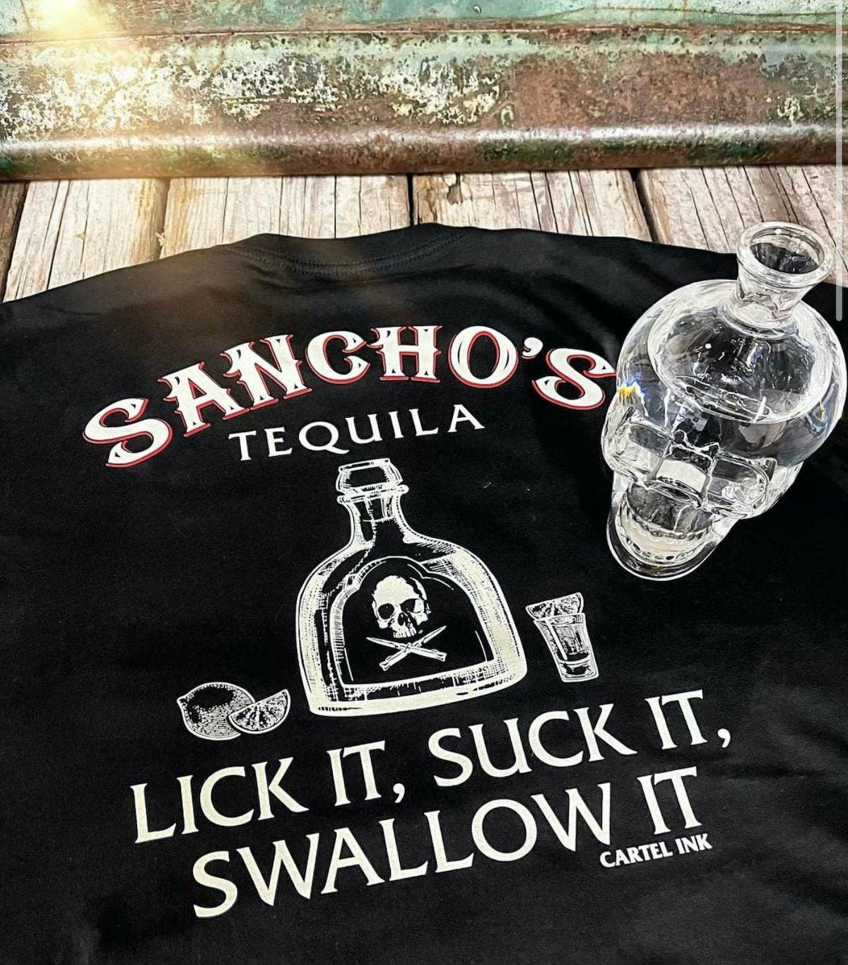 Black t-shirt with 'Sancho's Tequila' design and skull bottle graphic on a wooden surface.