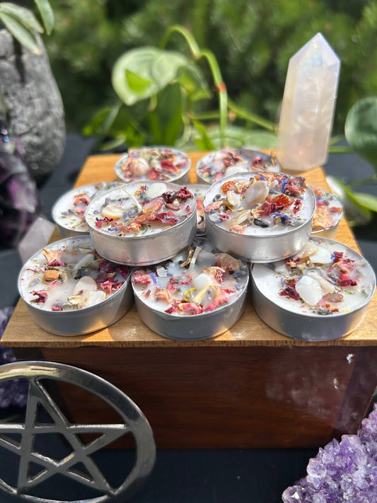 Small metal containers with decorative elements on a wooden surface, surrounded by greenery and crystals.