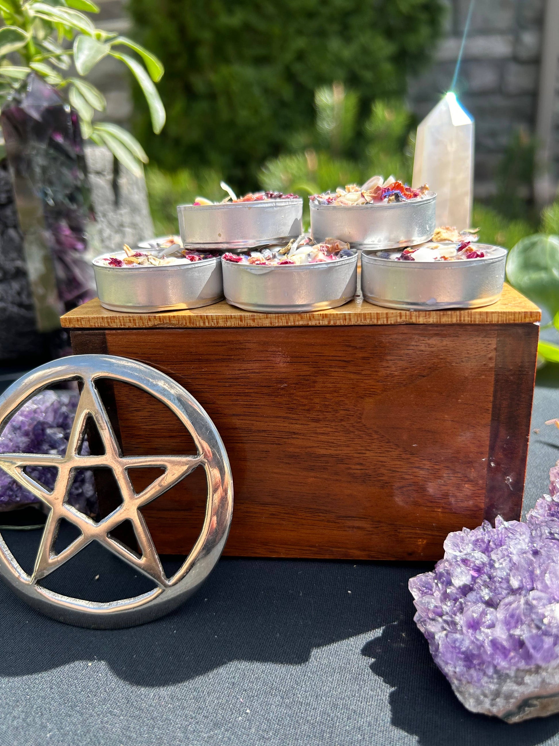 Small metal containers with floral elements on a wooden stand, surrounded by amethyst crystals and a pentagram symbol.