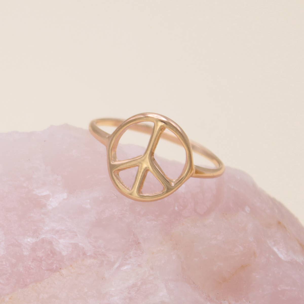 Gold peace sign ring on a pink stone with a beige background