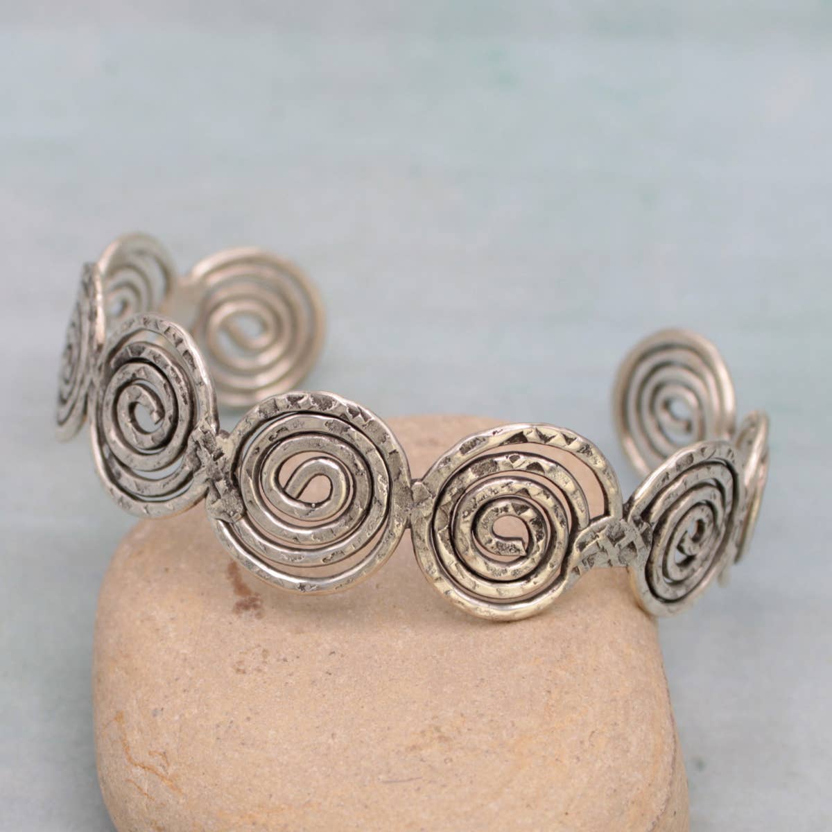Silver spiral bracelet on a stone with a light blue background