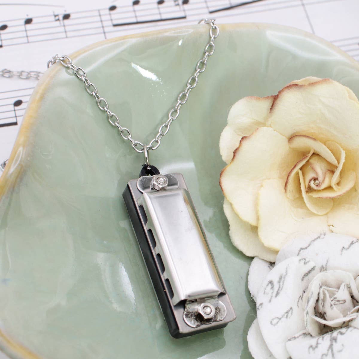 Harmonica necklace on a green plate with flowers and sheet music in the background