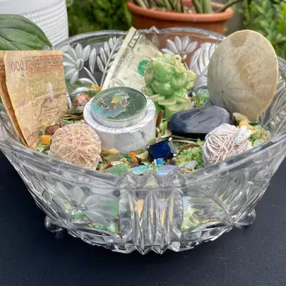 Crystal bowl with decorative stones, crystals, and a small figurine on a dark surface.