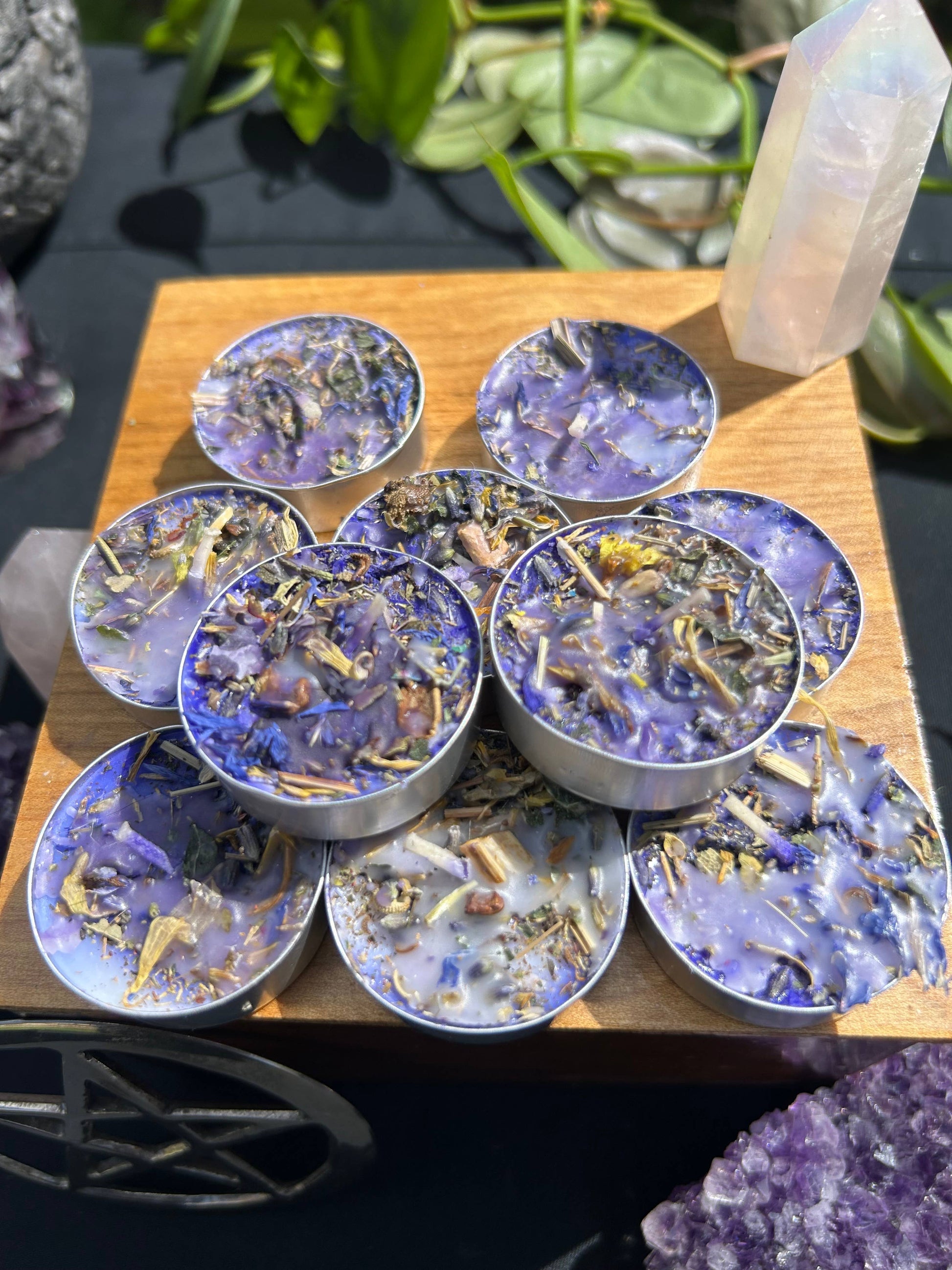 Set of small round containers with decorative elements on a wooden surface, surrounded by crystals and plants.