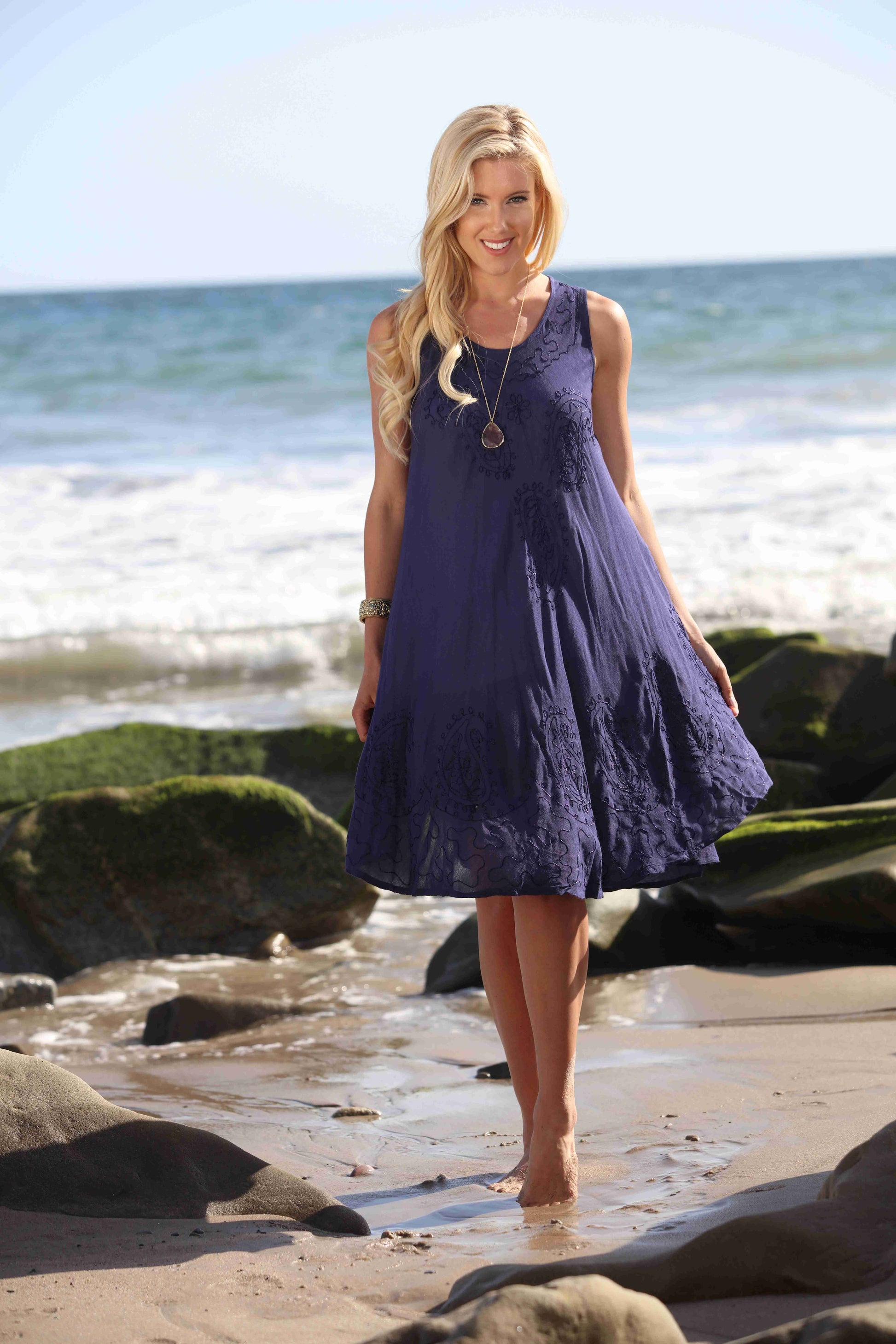 Woman in a blue dress standing on a beach with ocean waves in the background