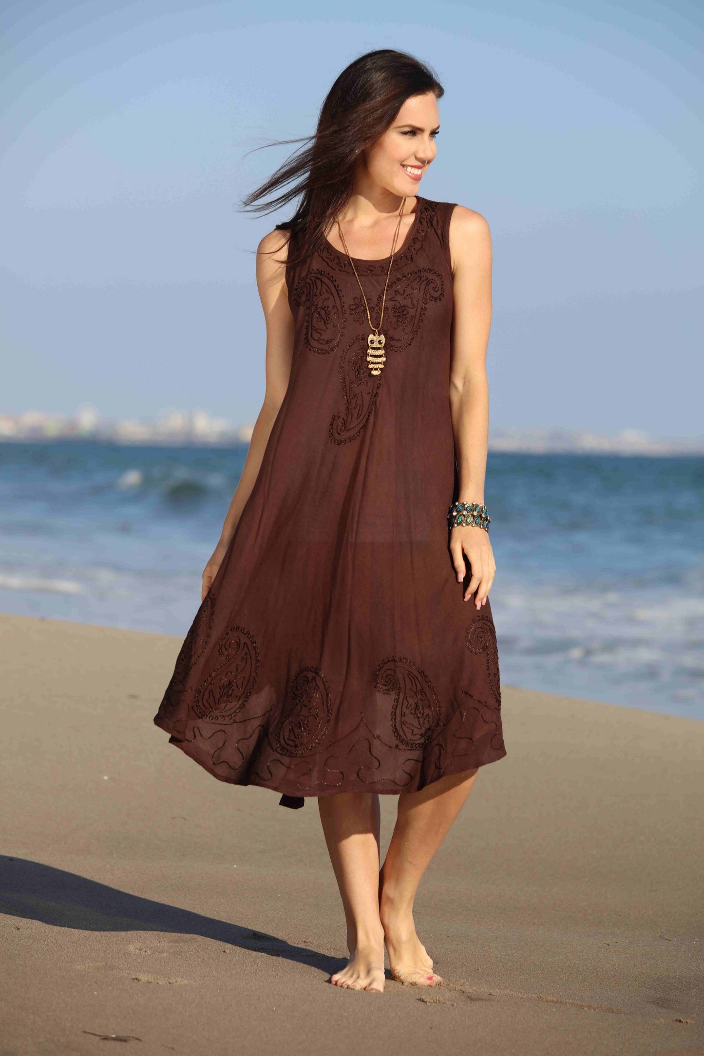 Woman in a brown dress standing on a beach with ocean in the background