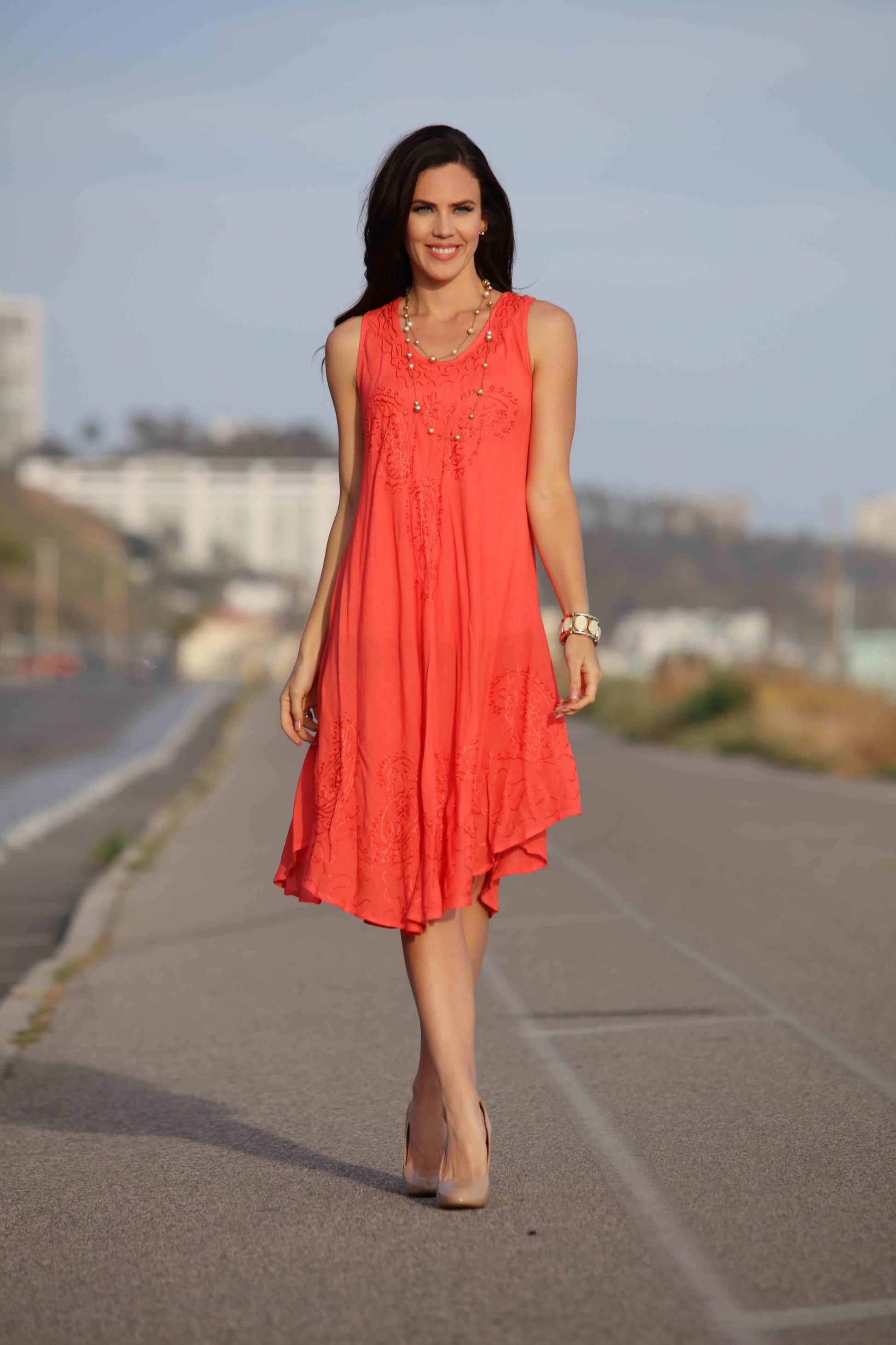Woman in a red dress walking on a road with buildings in the background