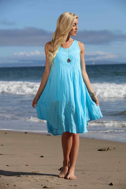 Woman in a blue dress standing on a beach with ocean waves in the background