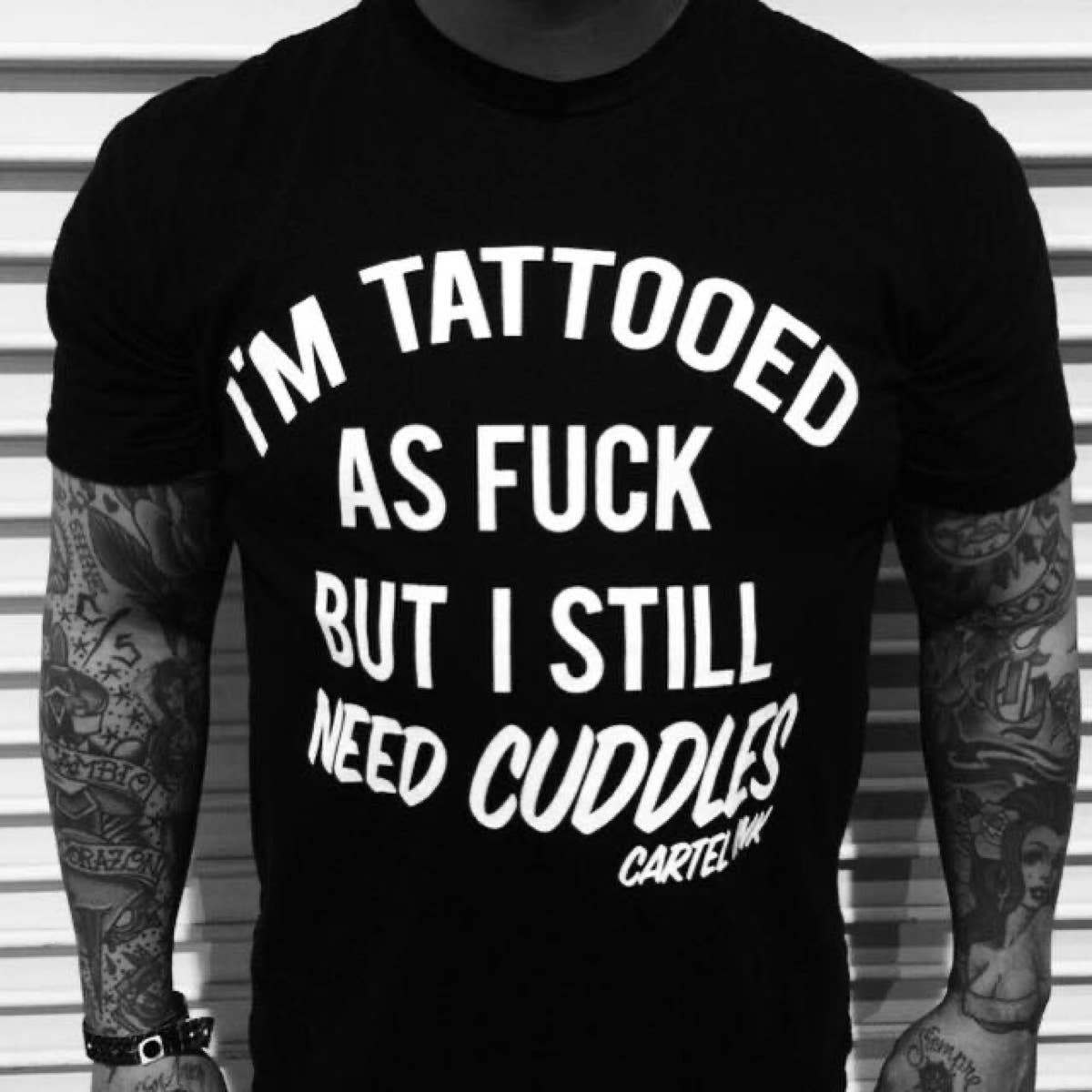 Person wearing a black t-shirt with white text and tattoos on arms.
