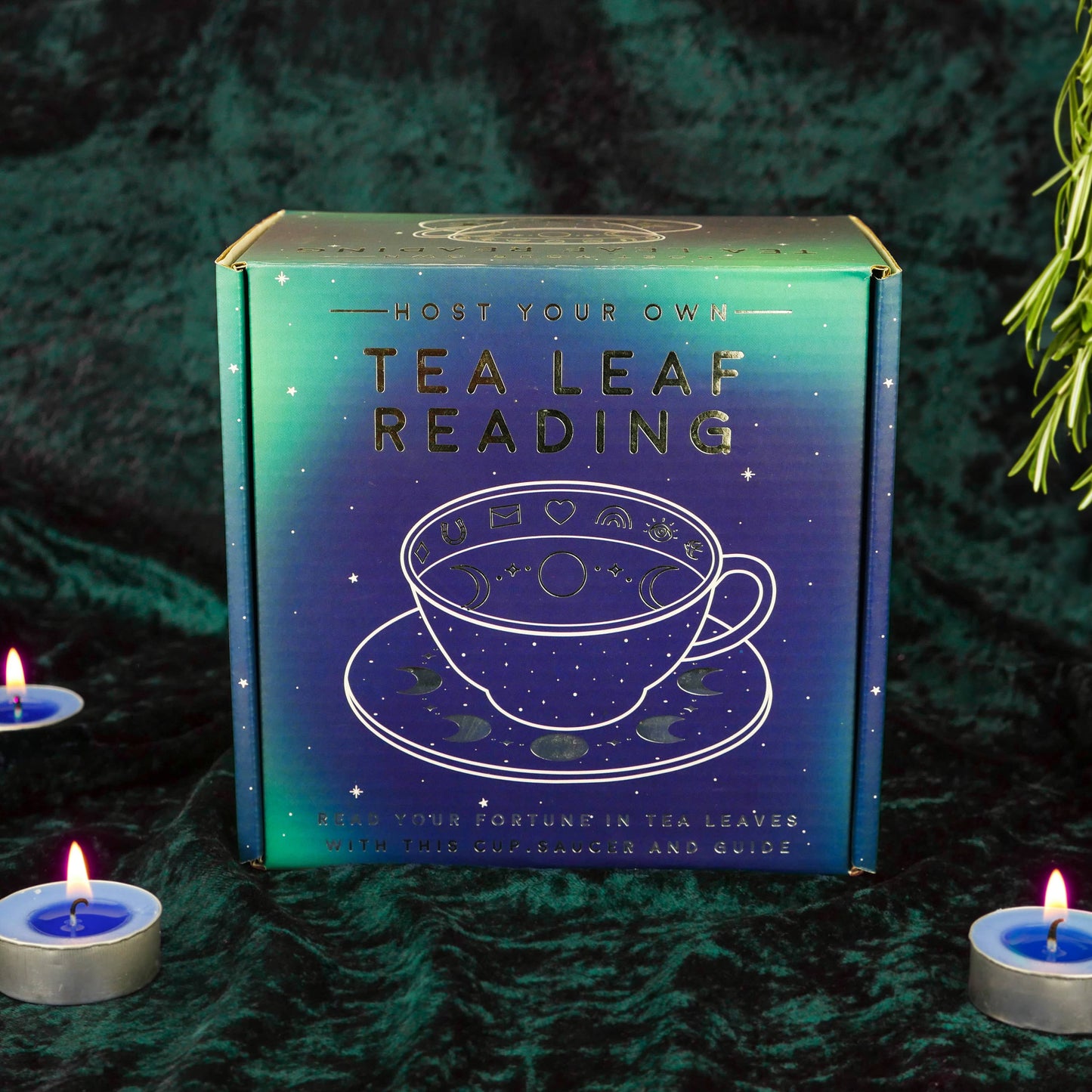 Tea leaf reading kit box with tea cup illustration on a dark background with candles.