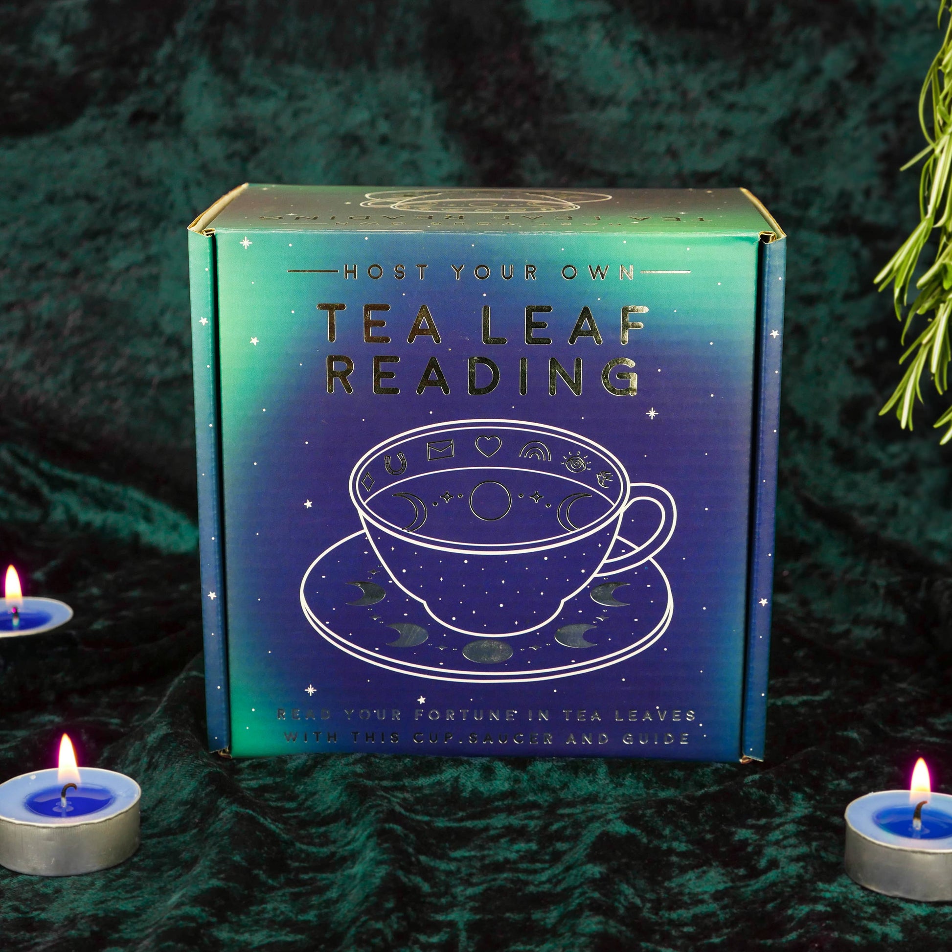 Tea leaf reading kit box with tea cup illustration on a dark background with candles.