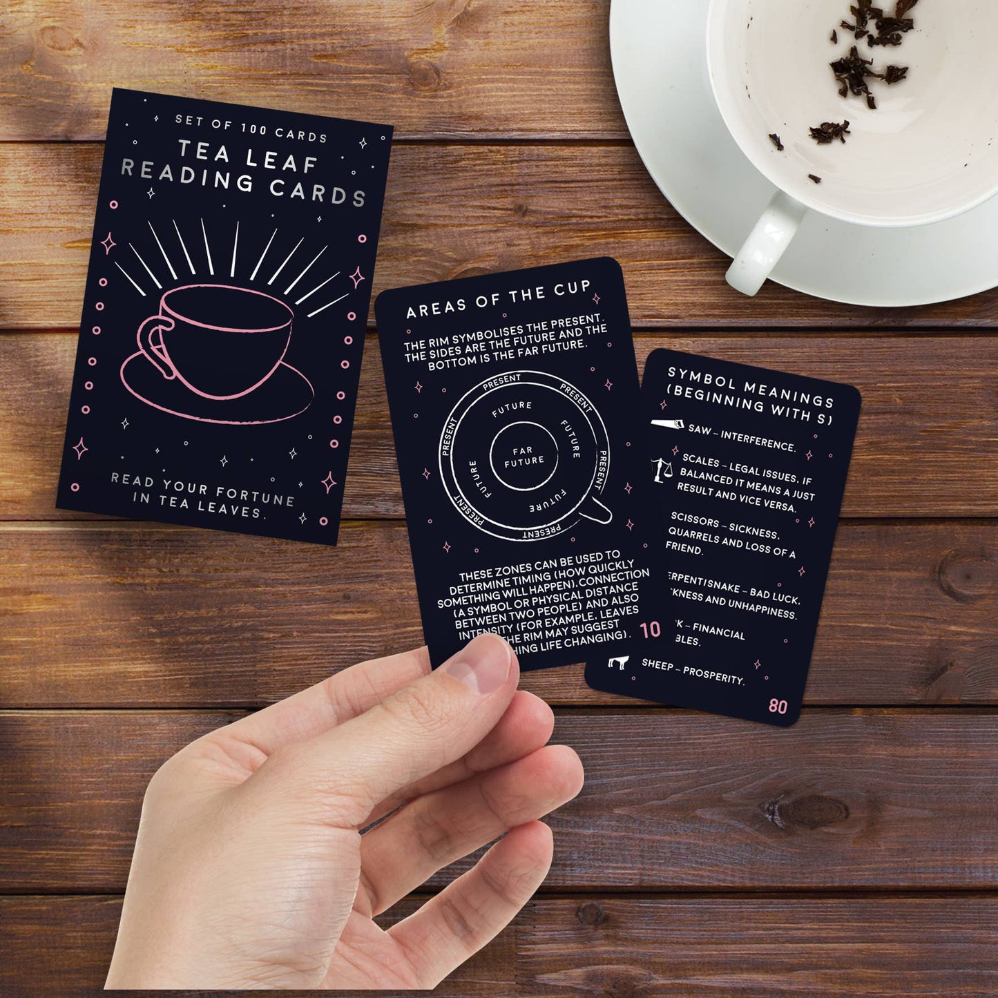Tea leaf reading cards on a wooden surface with a hand holding one card.