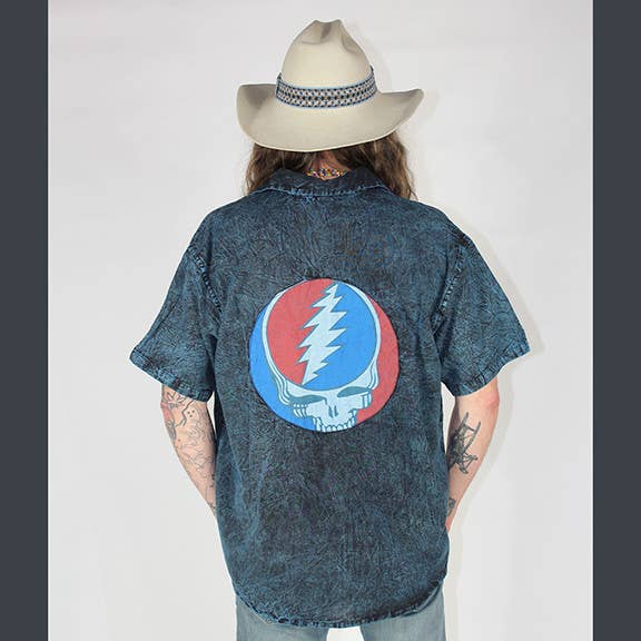 Person wearing a denim shirt with a Grateful Dead logo, standing against a plain background