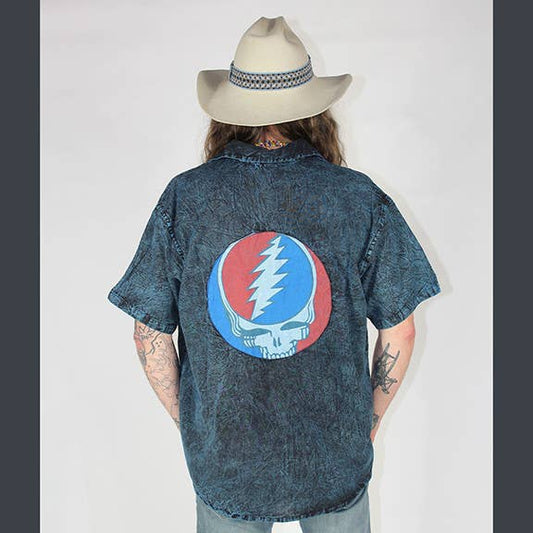 Person wearing a denim shirt with a Grateful Dead logo, standing against a plain background