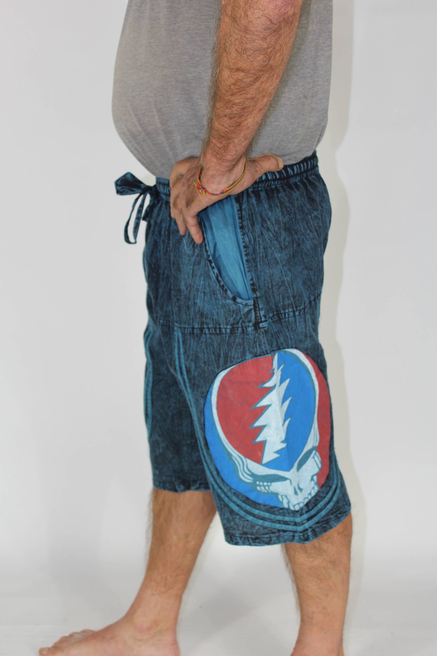 Person wearing blue denim shorts with a Grateful Dead logo on a plain background